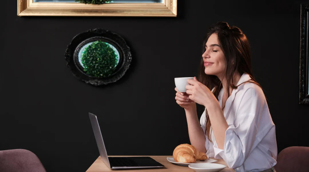 A woman at a table with a laptop and a coffee cup, showcasing the ideal coffee mug as a thoughtful gift for all.